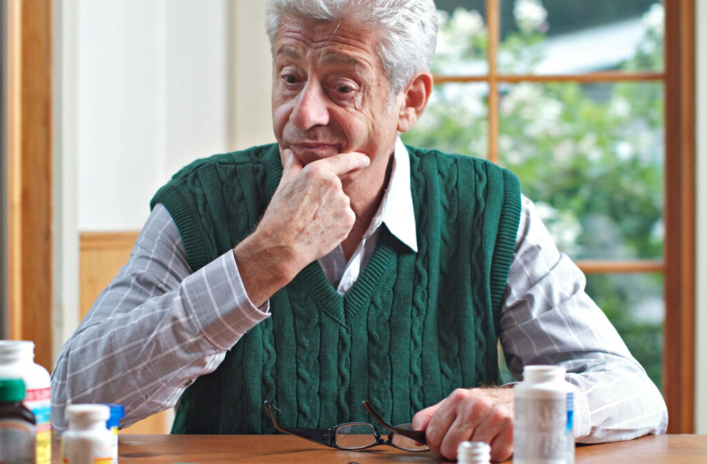 A senior man sitting at a table and looking at a few bottles of medication as if trying to make a decision.