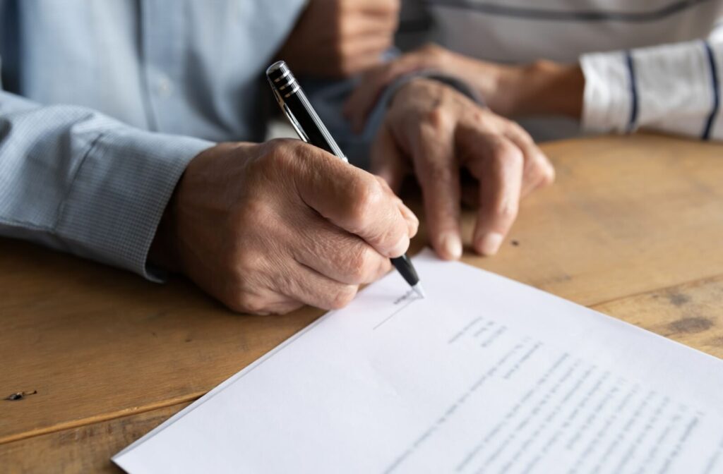 Close-up of an older adult man's right hand, holding a pen and signing a legal paper