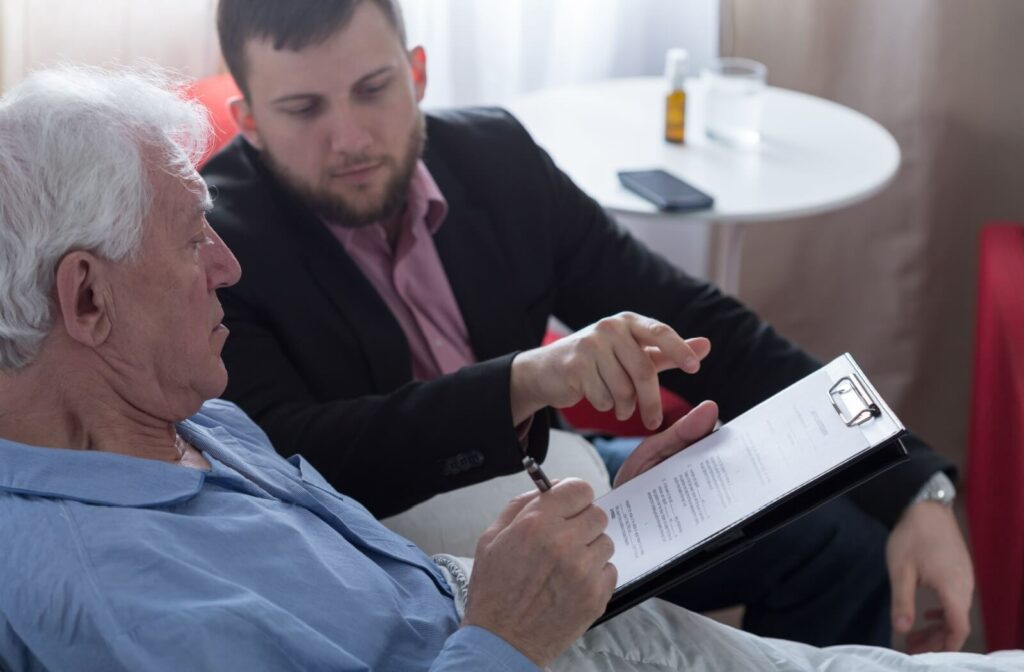 An older adult man holds a piece of paper while his lawyer talks about what's written on it.