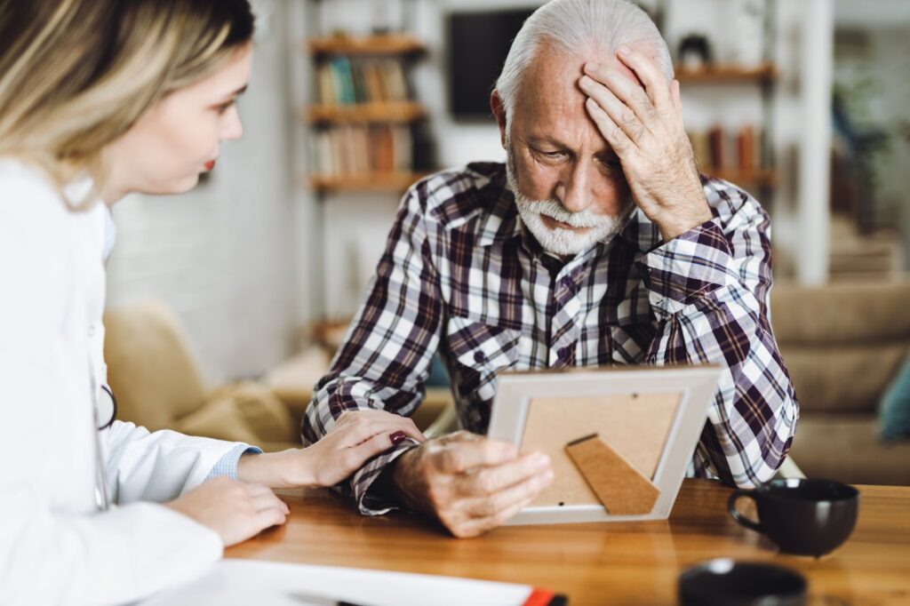 A family caregiver comforting an elderly parent with memory impairment while he looks at a photo frame.